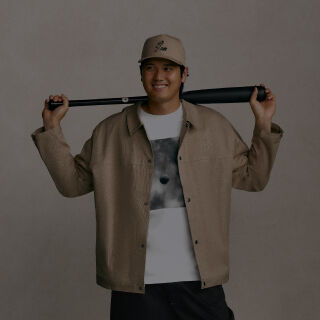 Ohtani standing and holding a baseball bat behind his head wearing a tan jacket