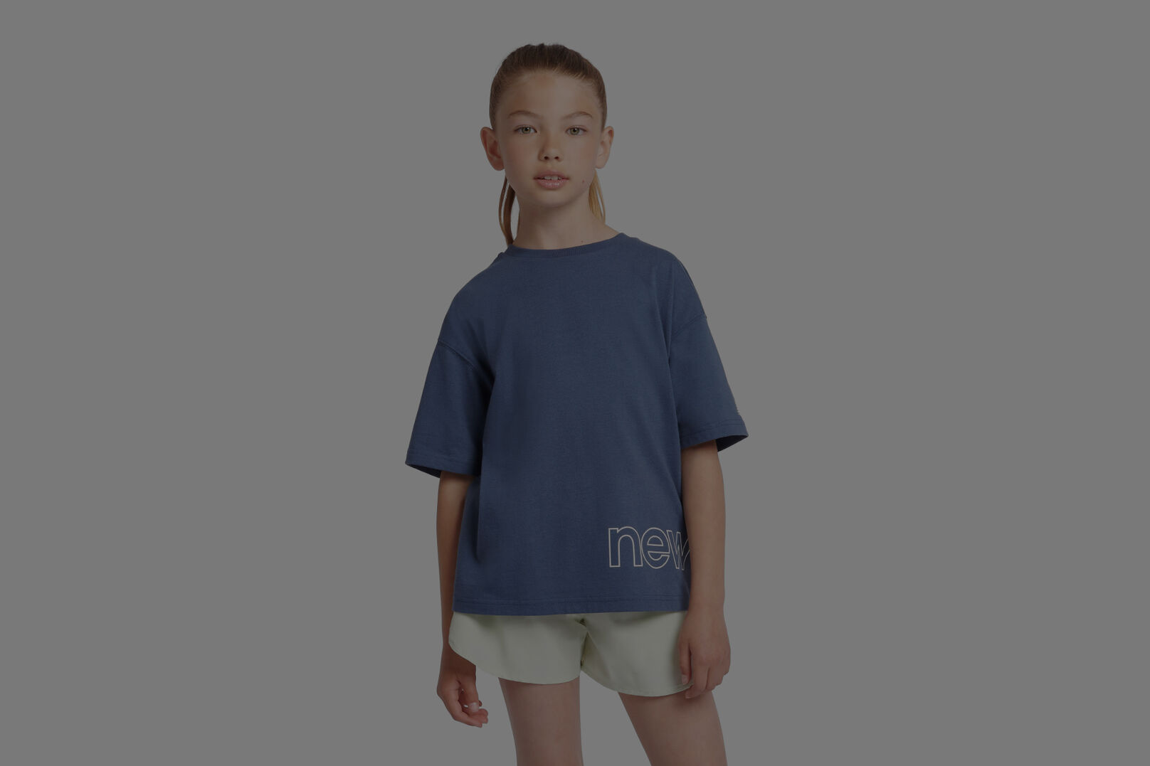 Child wearing blue New Balance shirt with grey background.