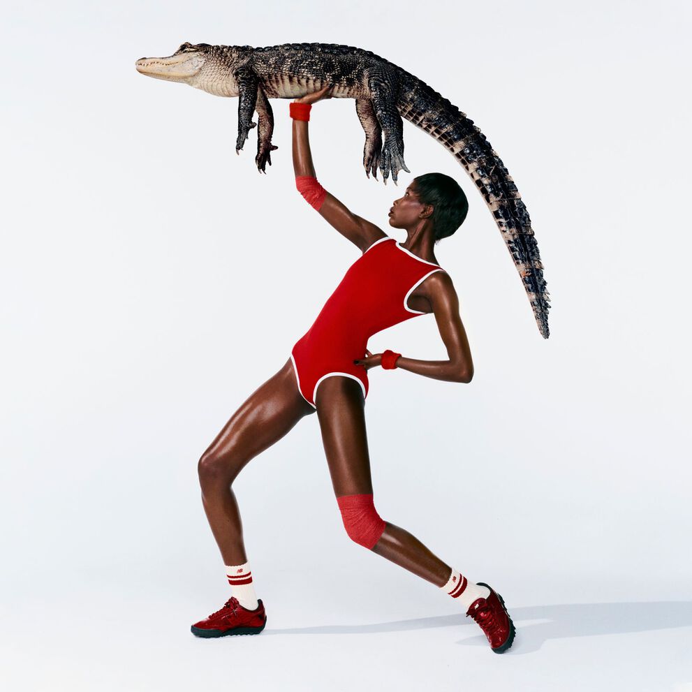 A woman in front of a white background wearing Gator Run shoes while holding an alligator.