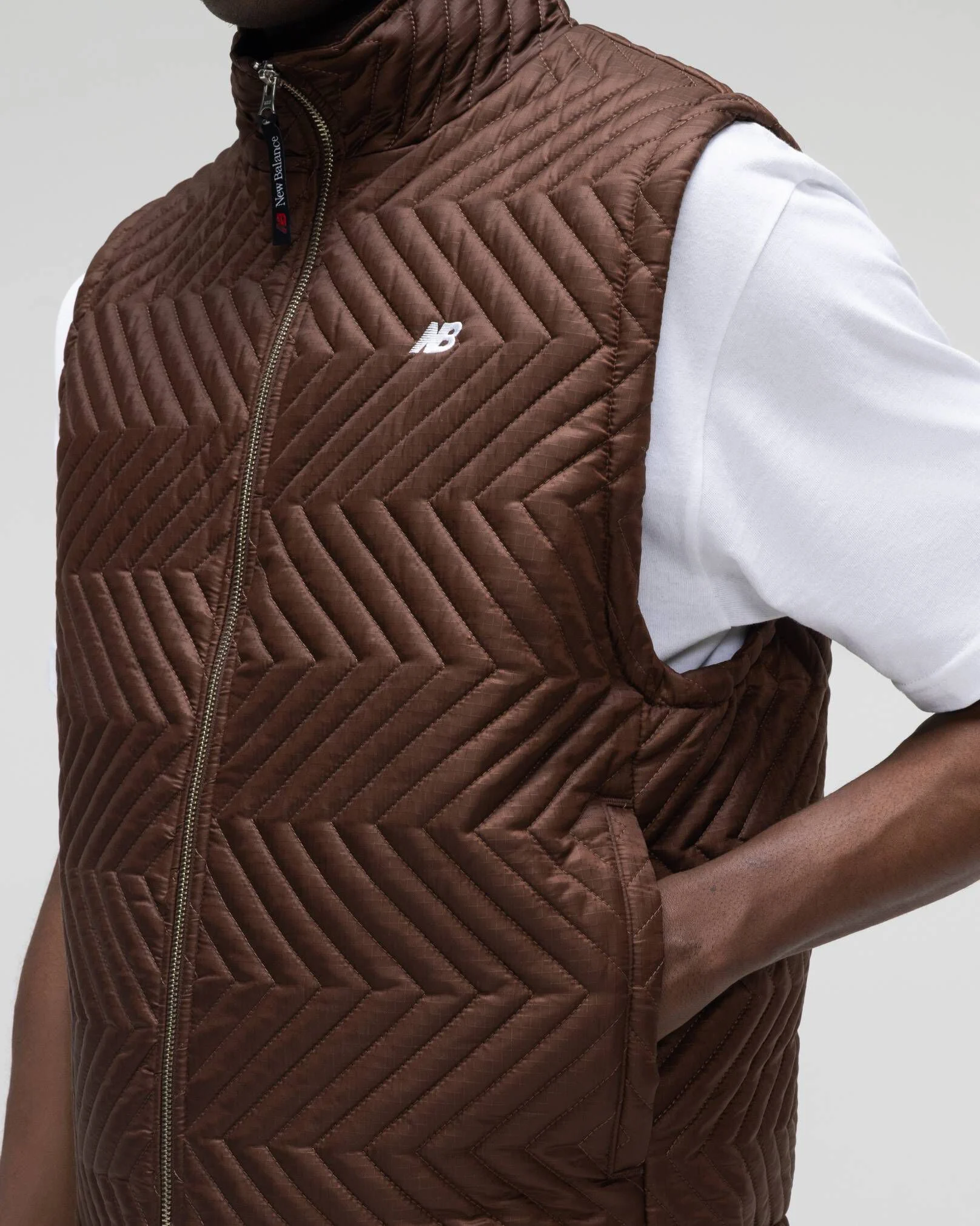 A person wearing a brown vest standing in front of a grey studio backdrop