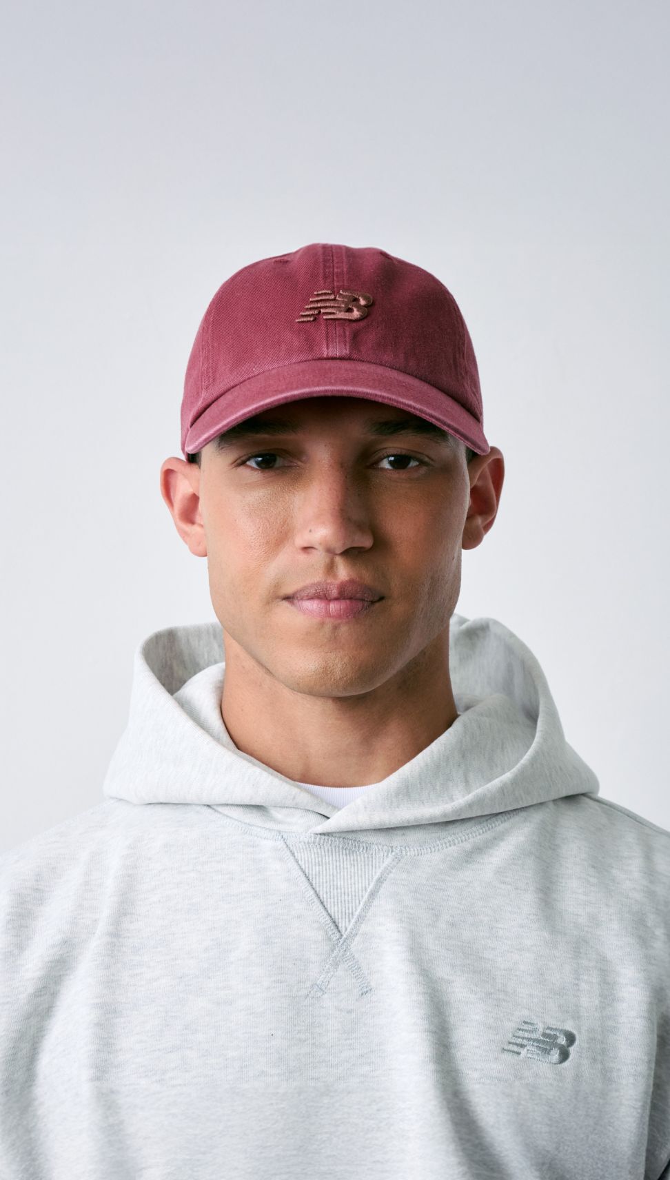 Hombre con gorra New Balance de pie frente a una pared blanca