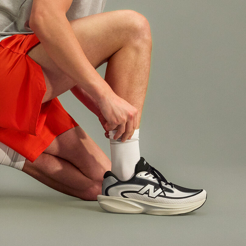 Close-up studio image of a person kneeling on one knee against a smooth, neutral gray background.