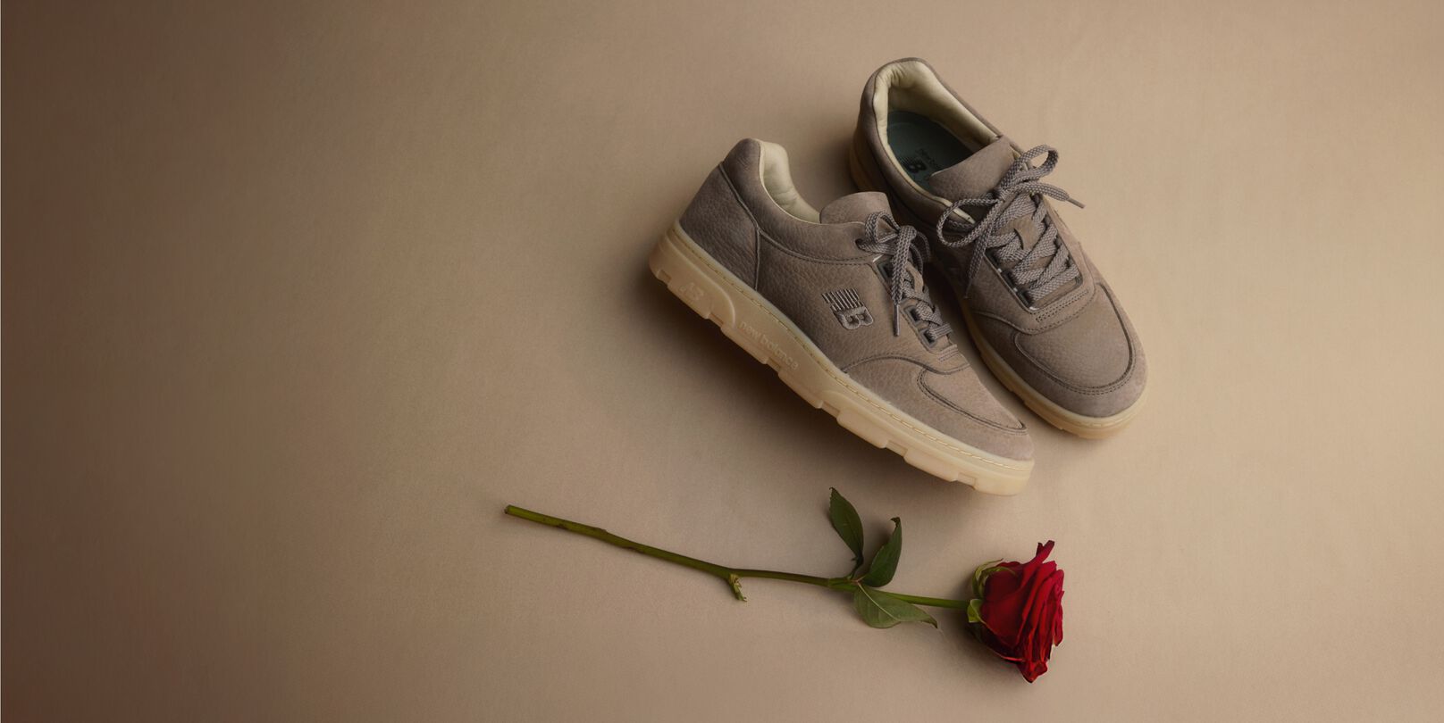 Unas zapatillas New Balance Made in UK sobre un suelo beige junto a una singular rosa roja. 
