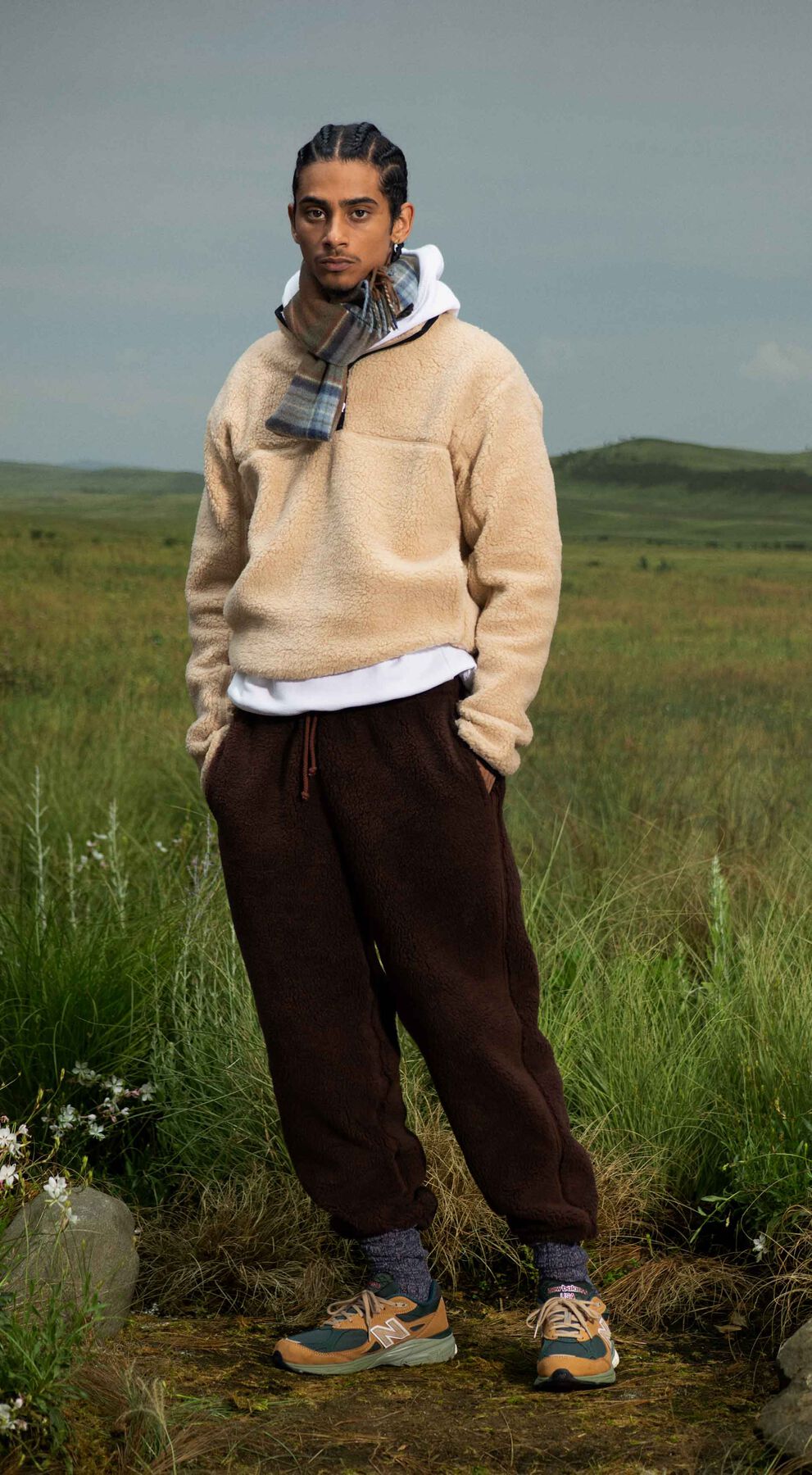 A man standing in a beautiful outdoor environment wearing the tan and green 990v3 sneakers.