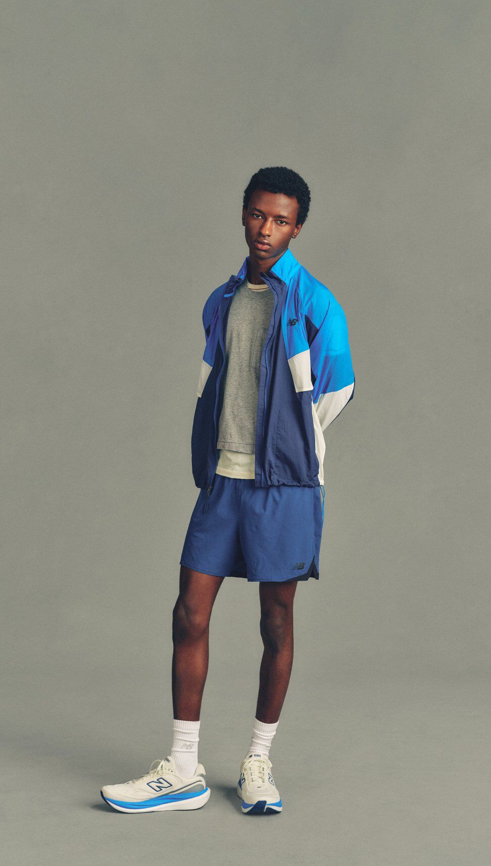 The person is wearing a coordinated athletic outfit consisting of a blue and purple color-blocked zip-up jacket layered over a light gray T-shirt, paired with blue running shorts.
