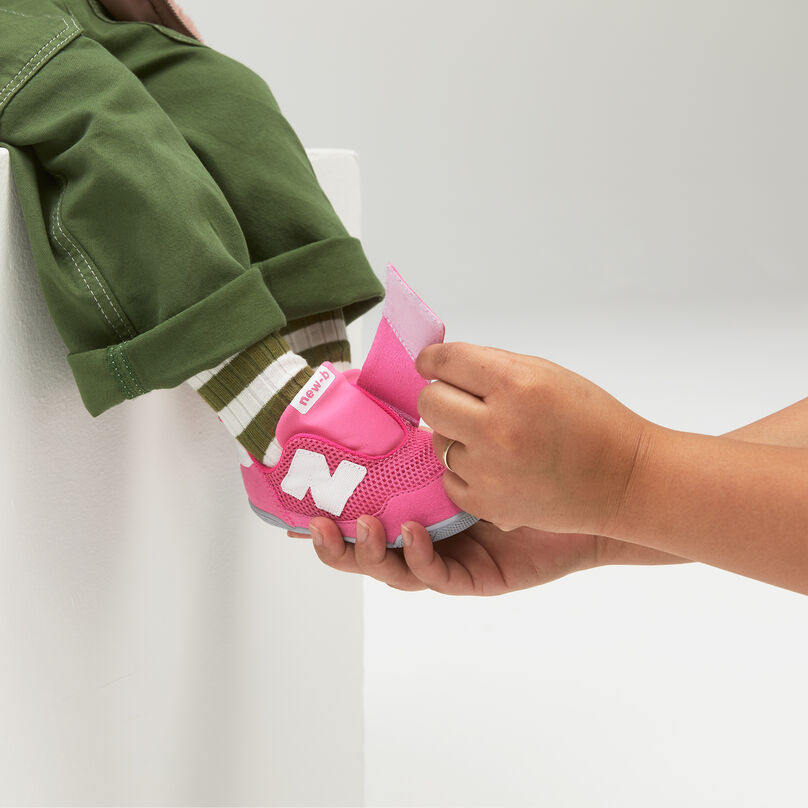 Adult helping a child secure pink velcro New-B shoes