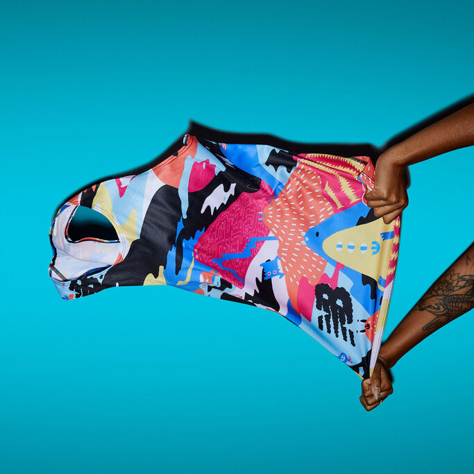 Person cropped at the arms holding colorful singlet against a blue background 