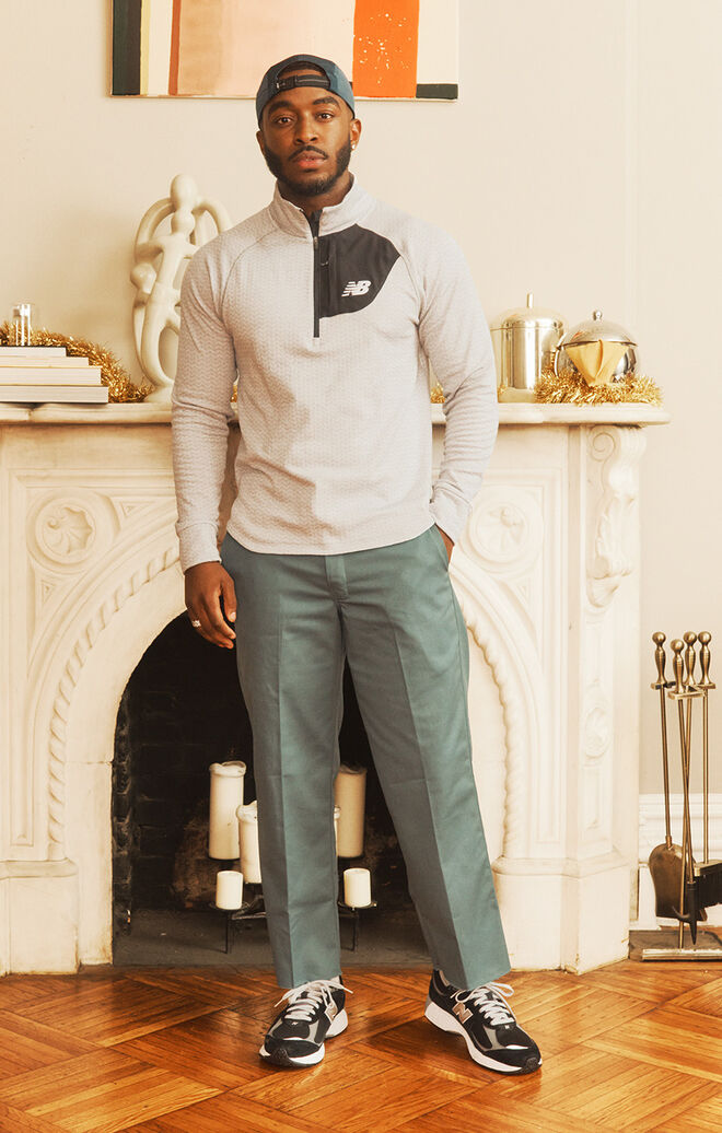 Male model wearing cold weather New Balance clothing and shoes posed against a decorative fireplace