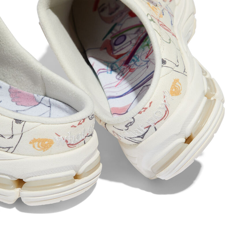 The heel of a pair of cream colored mule shoes with embroidered art on the shoe