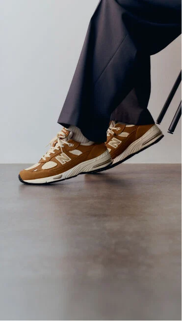 Knee down view of a man wearing a pair of New Balance Made in UK sneakers in with room with a concrete floor and white walls. 