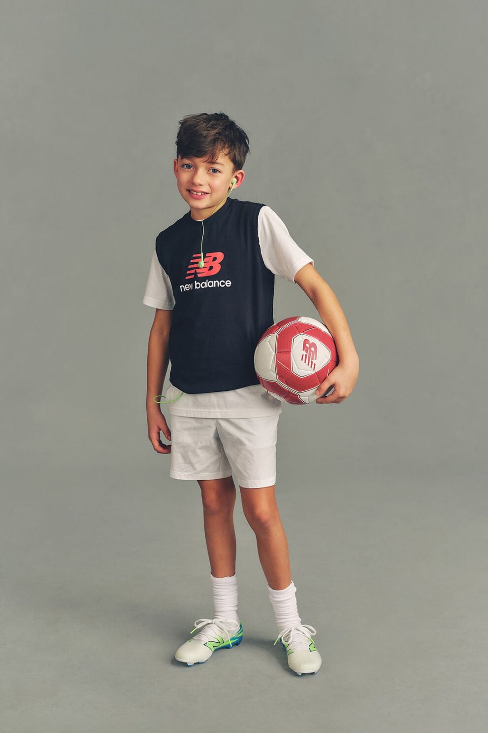 Kid holding a soccer ball against a grey studio background.