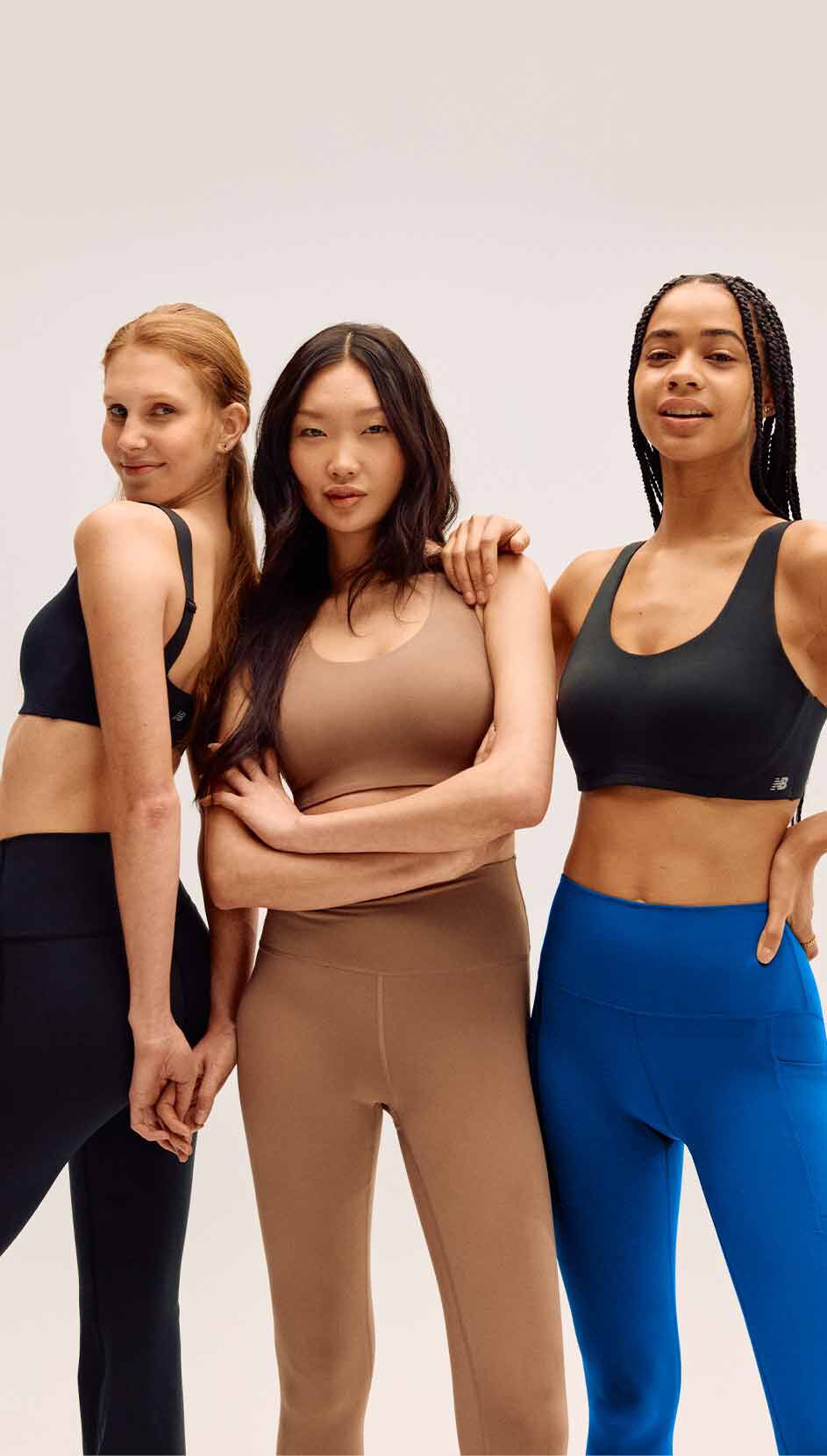 Three women wearing New Balance sports bras standing in front of a grey studio backdrop.