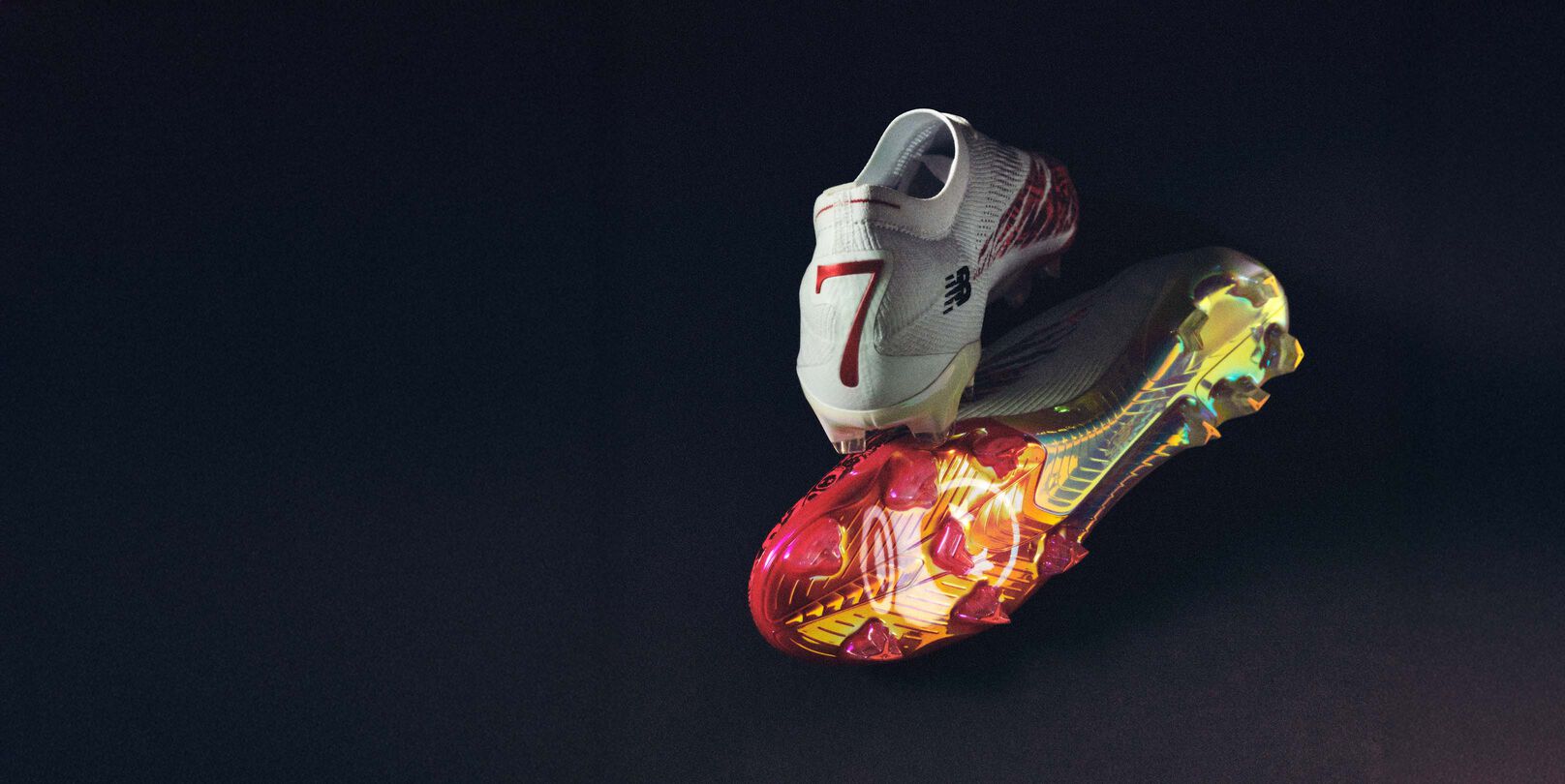 Pair of white soccer cleats with red accents and multicolor sole on a dark background.