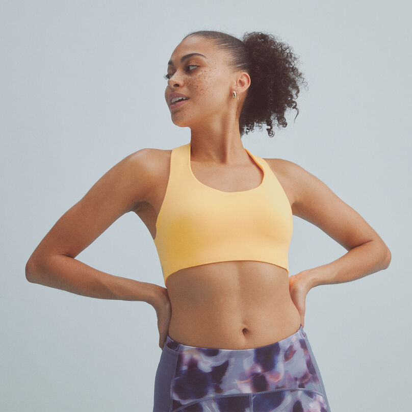 Woman wearing a yellow NB Fortiflow Bra with multi-colored leggings