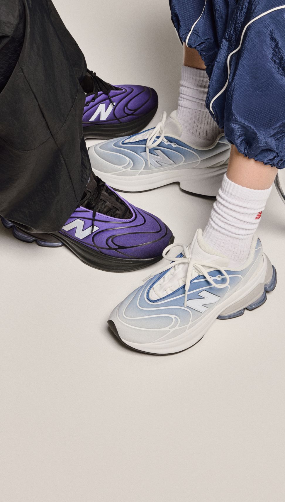 Knee-down view of two people wearing sneakers on a beige background. 
