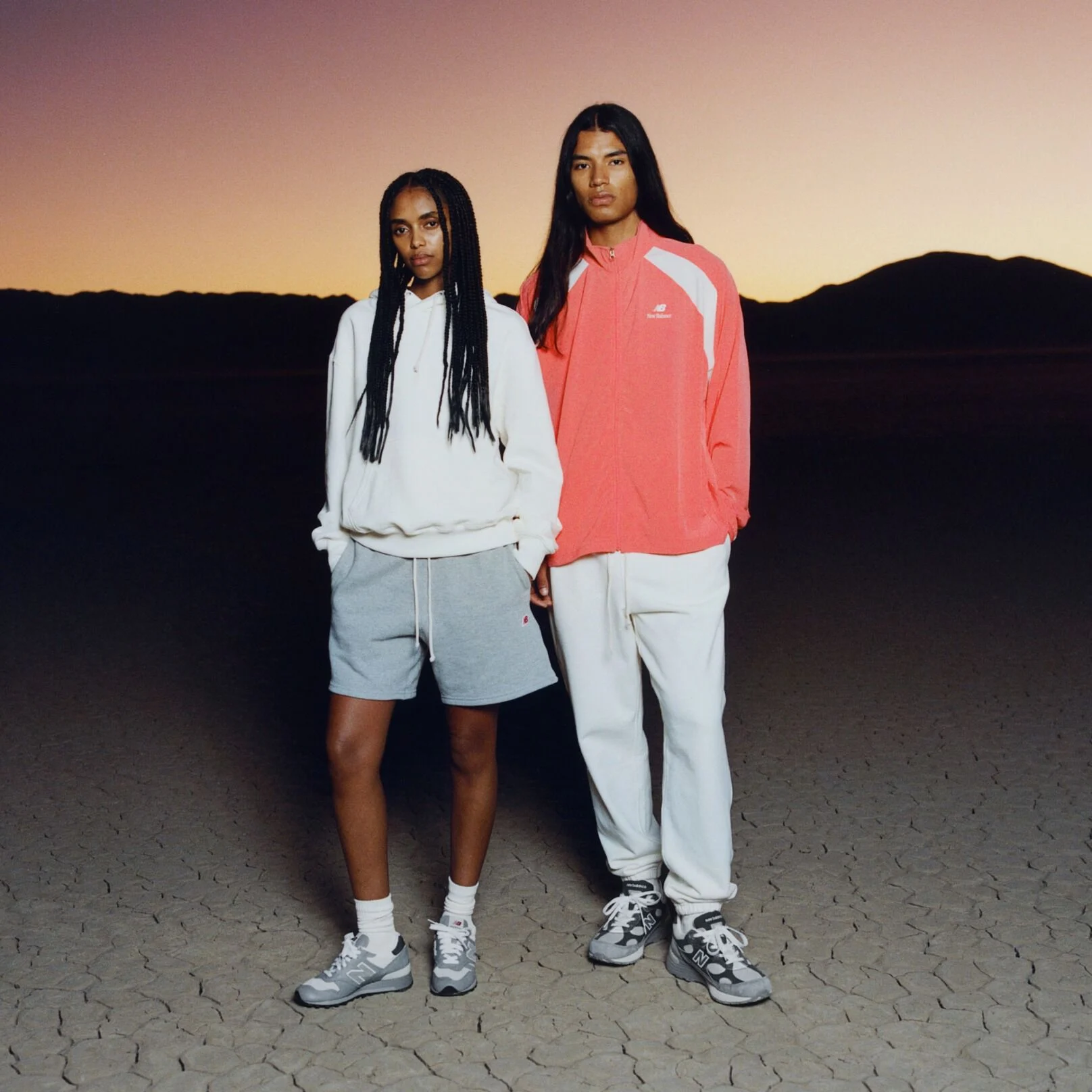 Two people with their hands in their pockets. One is wearing an orange jacket, the other is wearing a white hoodie. 