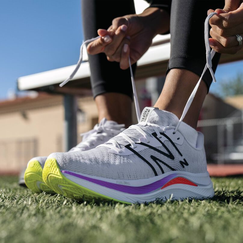 A  pair of white Fuelcell Propel shoes hanging on a bench in a field.  
