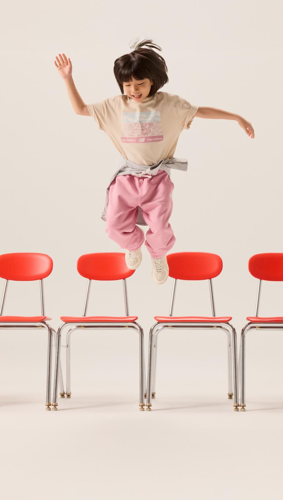 A young female in pink pants jumping off a chair. 