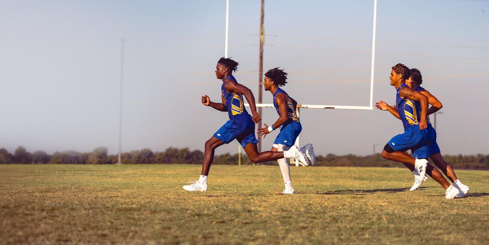 Atletas de fútbol americano de secundaria corriendo en un campo con tacos blancos de fútbol americano New Balance.