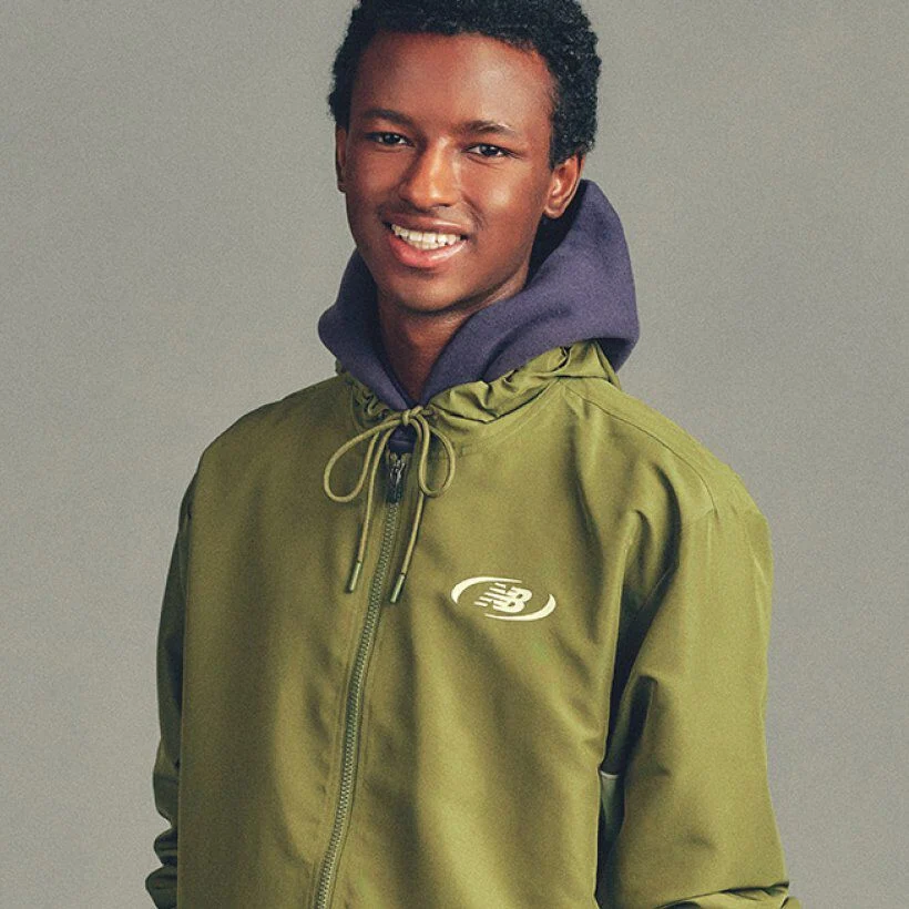 Close-up portrait of a person wearing a green New Balance jacket layered over a hoodie, standing against a plain background.