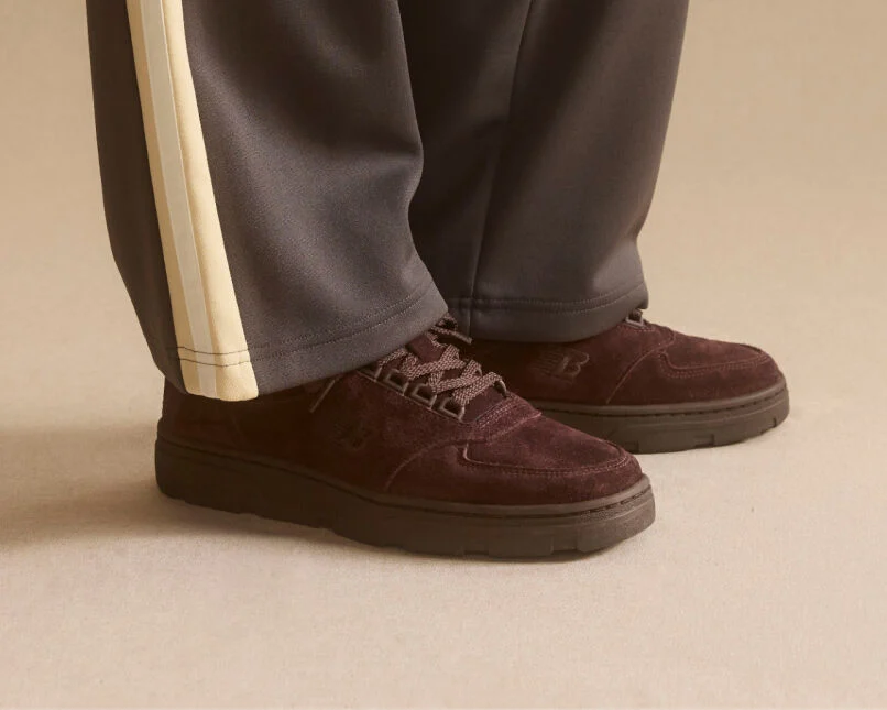 Knee down view of a woman wearing a pair of New Balance Made in UK sneakers standing in a beige studio environment.