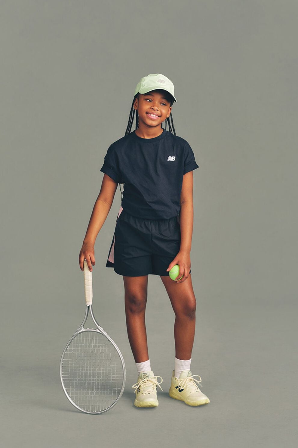 Kid holding a tennis racket against a grey studio background.