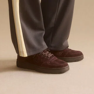 Knee down view of a woman wearing a pair of New Balance Made in UK sneakers standing in a beige studio environment.