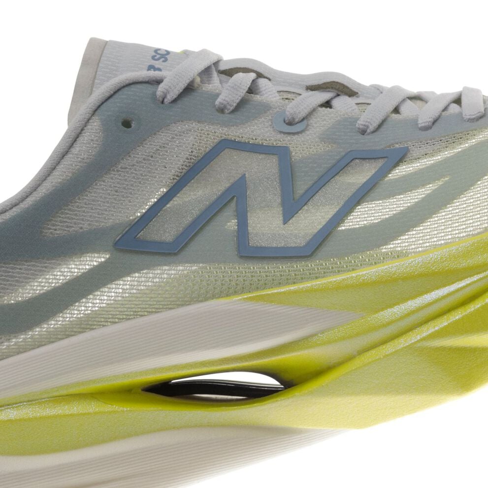 Close-up side view of a New Balance running shoe featuring a light gray mesh upper, blue &ldquo;N&rdquo; logo, white laces, and a lime-green sculpted midsole with a visible hollow cushioning design.