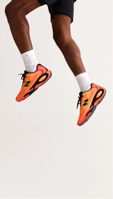 Waist down image of a person jumping wearing orange AC Runner shoes. 