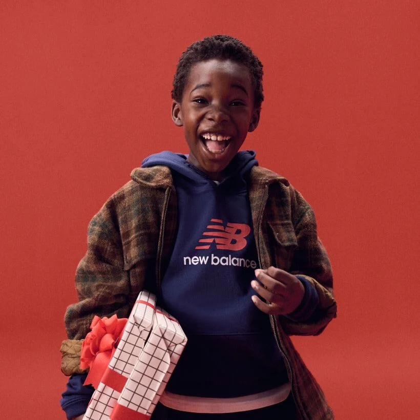 Young kid laughing while holding gifts on a red background.