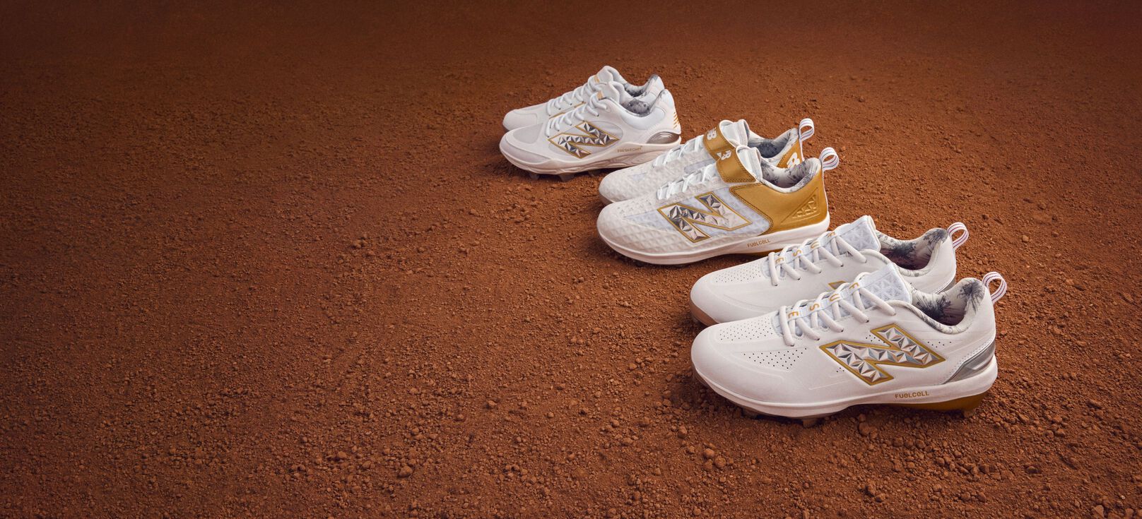 Three pair of gold and white cleats sitting on dirt. 
