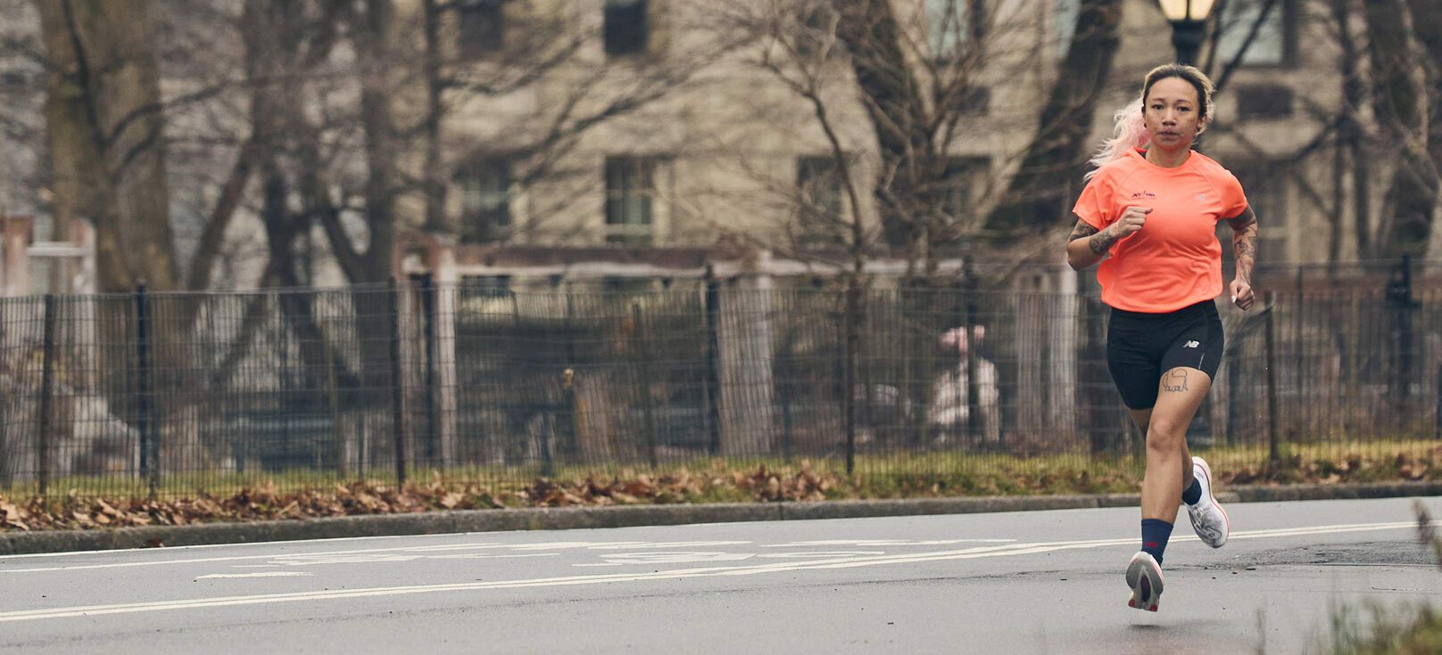 An individual in a orange New Balance shirt running in the city. 