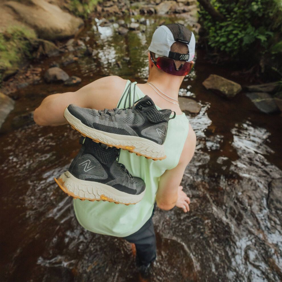 Person holding Fresh Foam X Hierro Mid shoes while walking in a river.