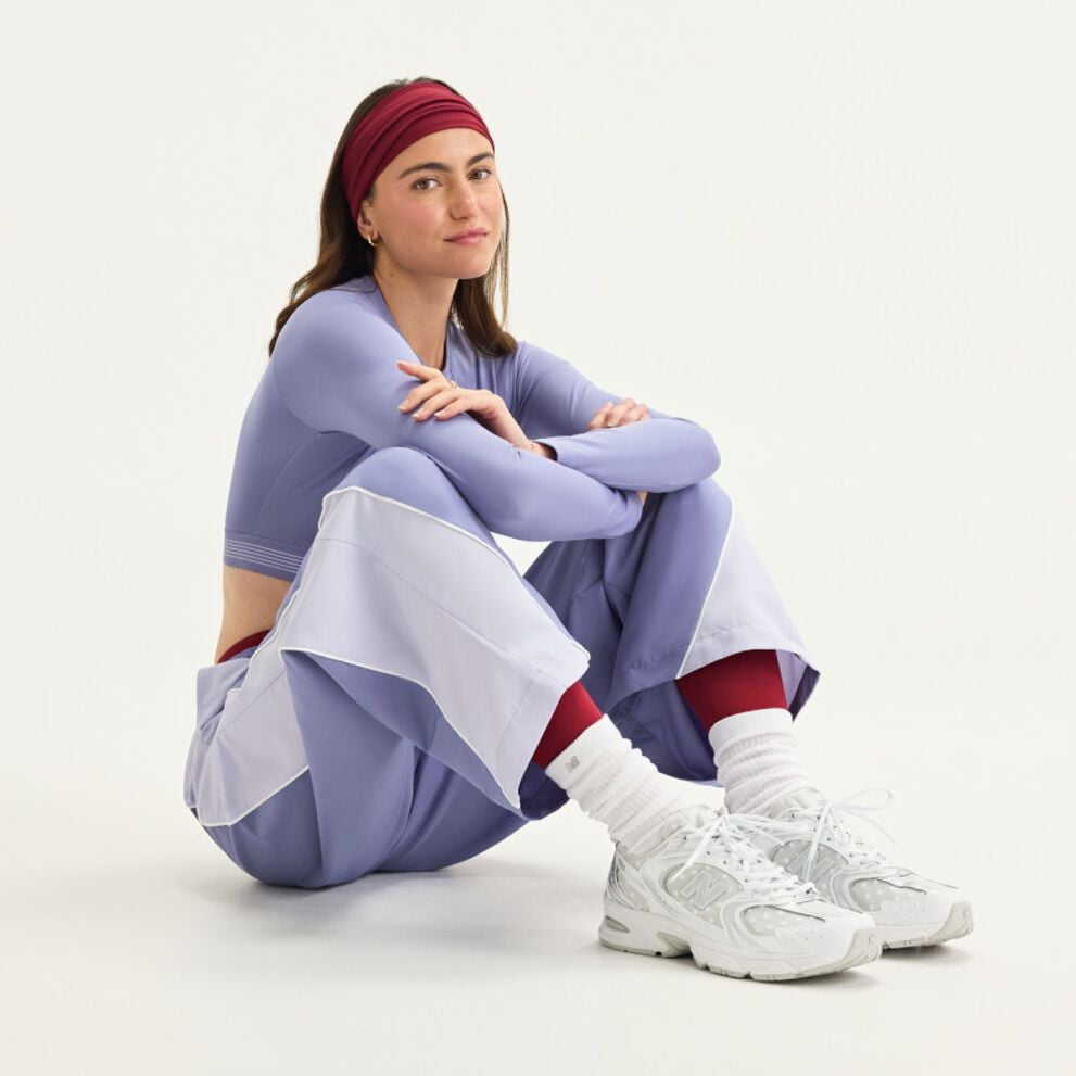 A woman sitting wearing New Balance gear on a white background.