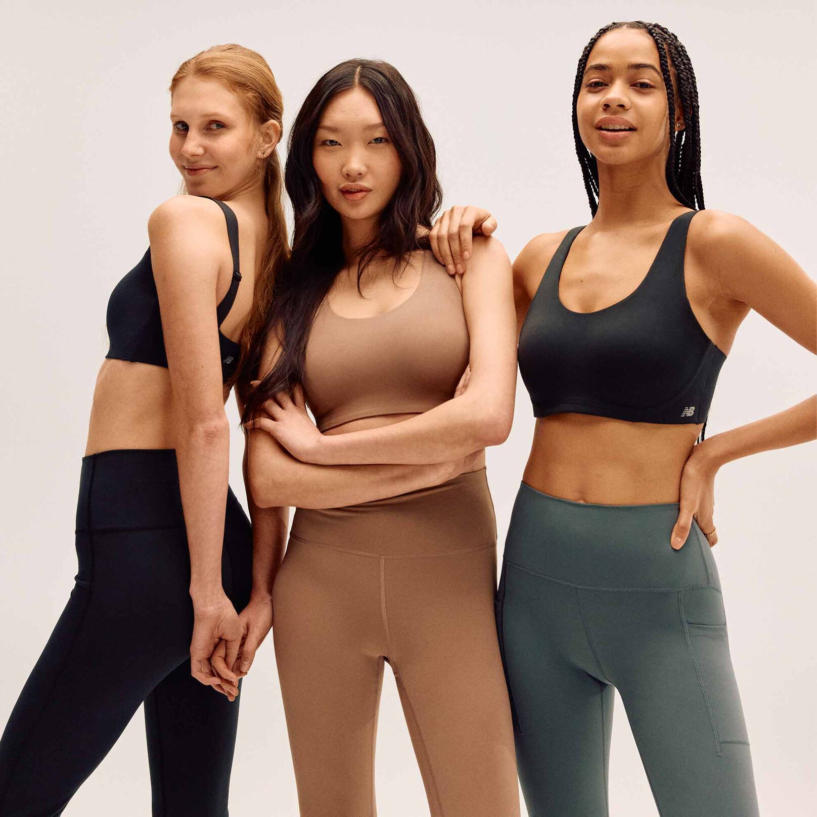A group of women wearing leggings and sports bras in front of a cream studio background. 