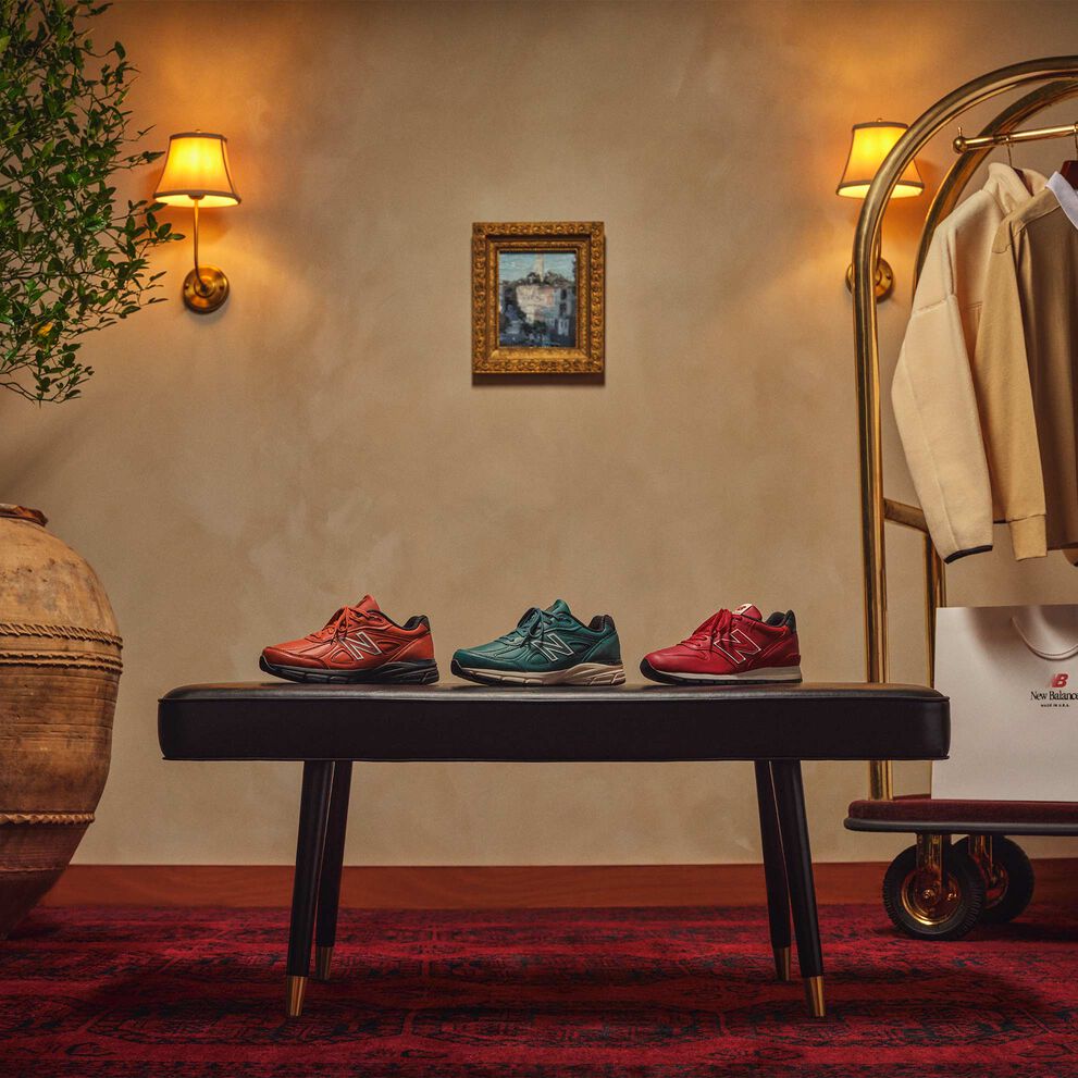 New Balance MADE in USA shoes, apparel, and boxes sitting or hanging on a gold luggage cart in a beautiful indoor environment. 