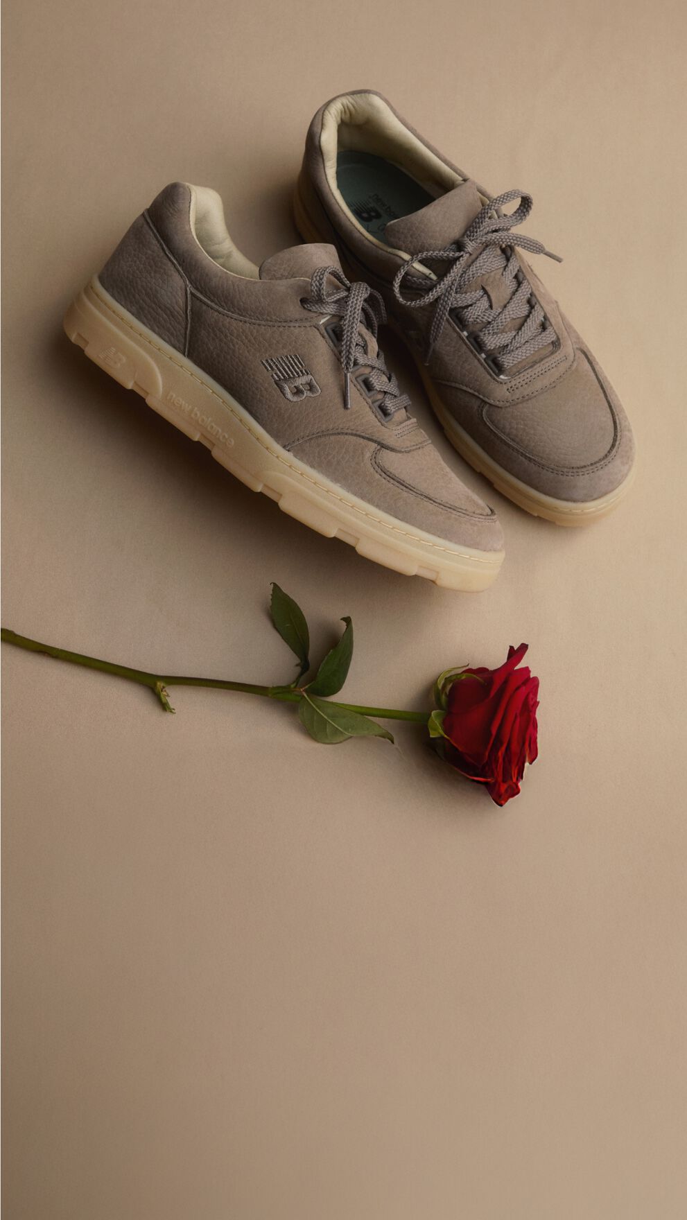 Unas zapatillas New Balance Made in UK sobre un suelo beige junto a una singular rosa roja. 
