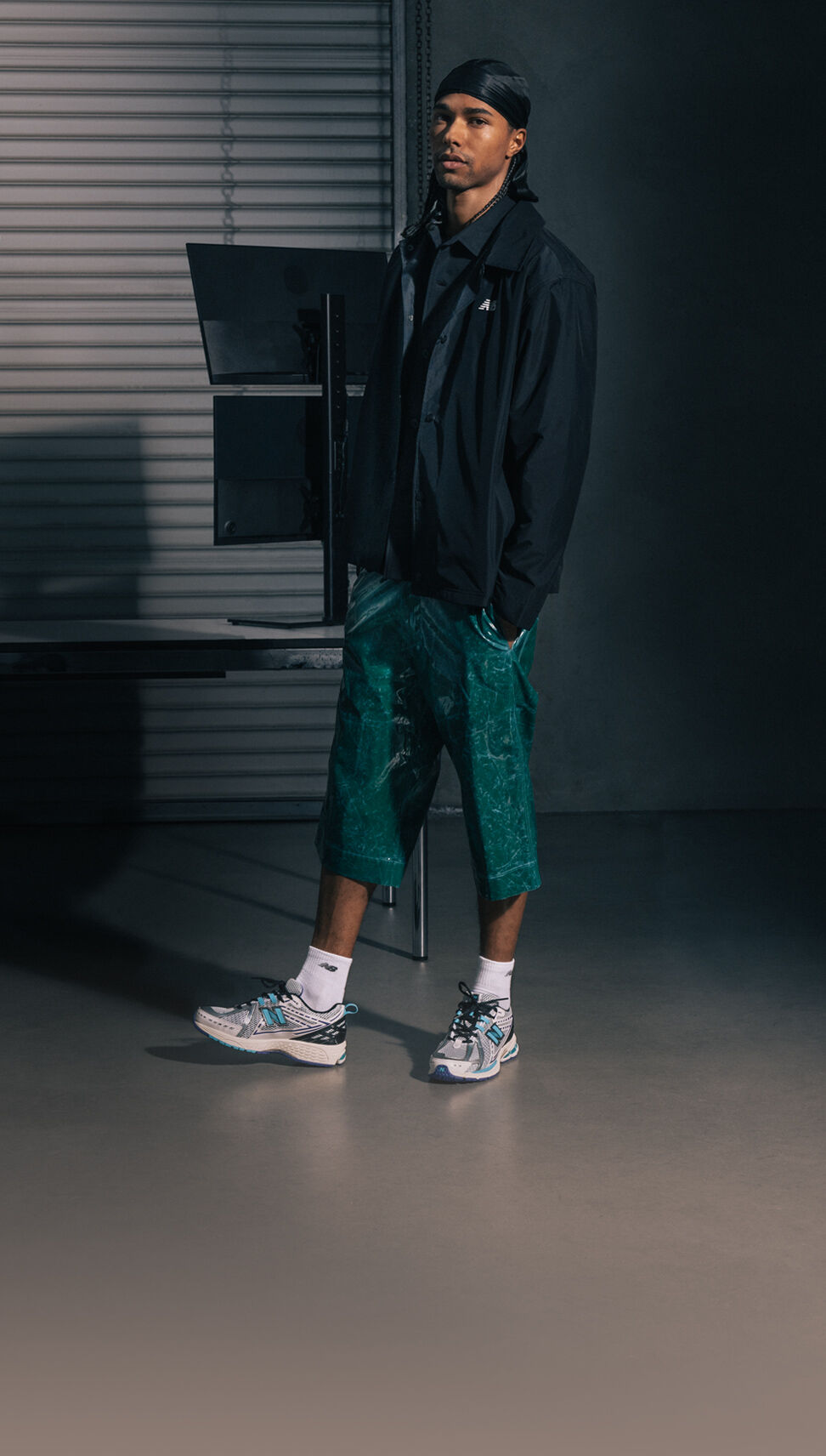 An individual wearing a black New Balance jacket, green shorts, and white New Balance 1906Rs.