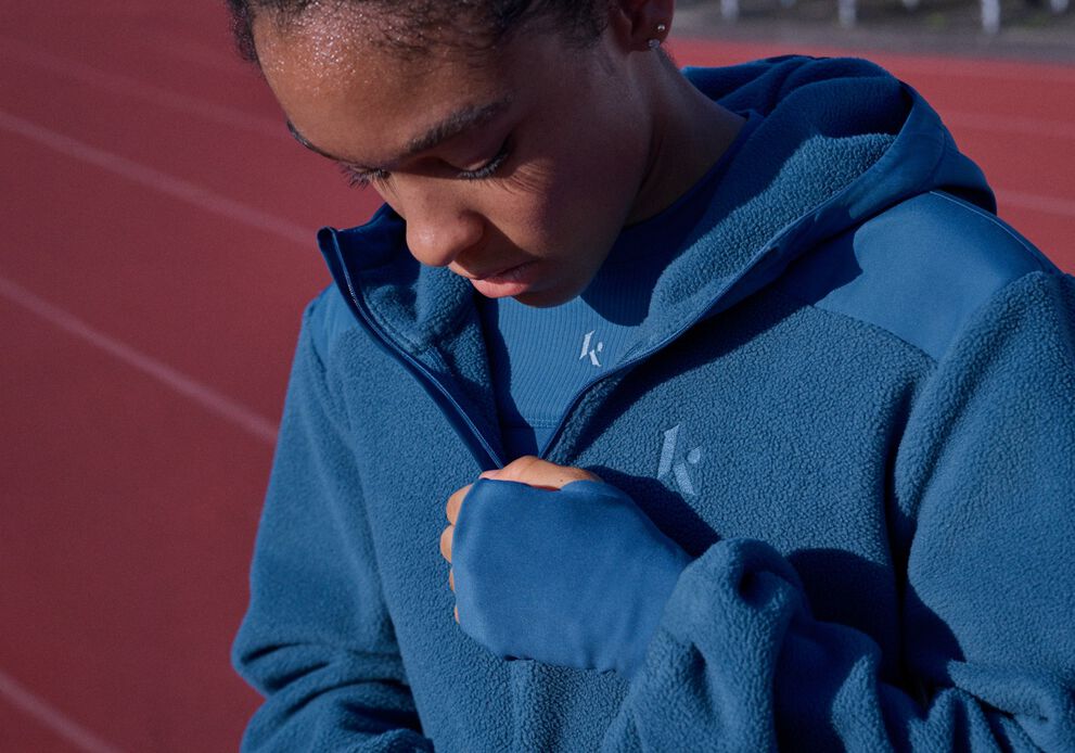 Close-up of an athlete wearing a blue fleece jacket and performance top on a running track.