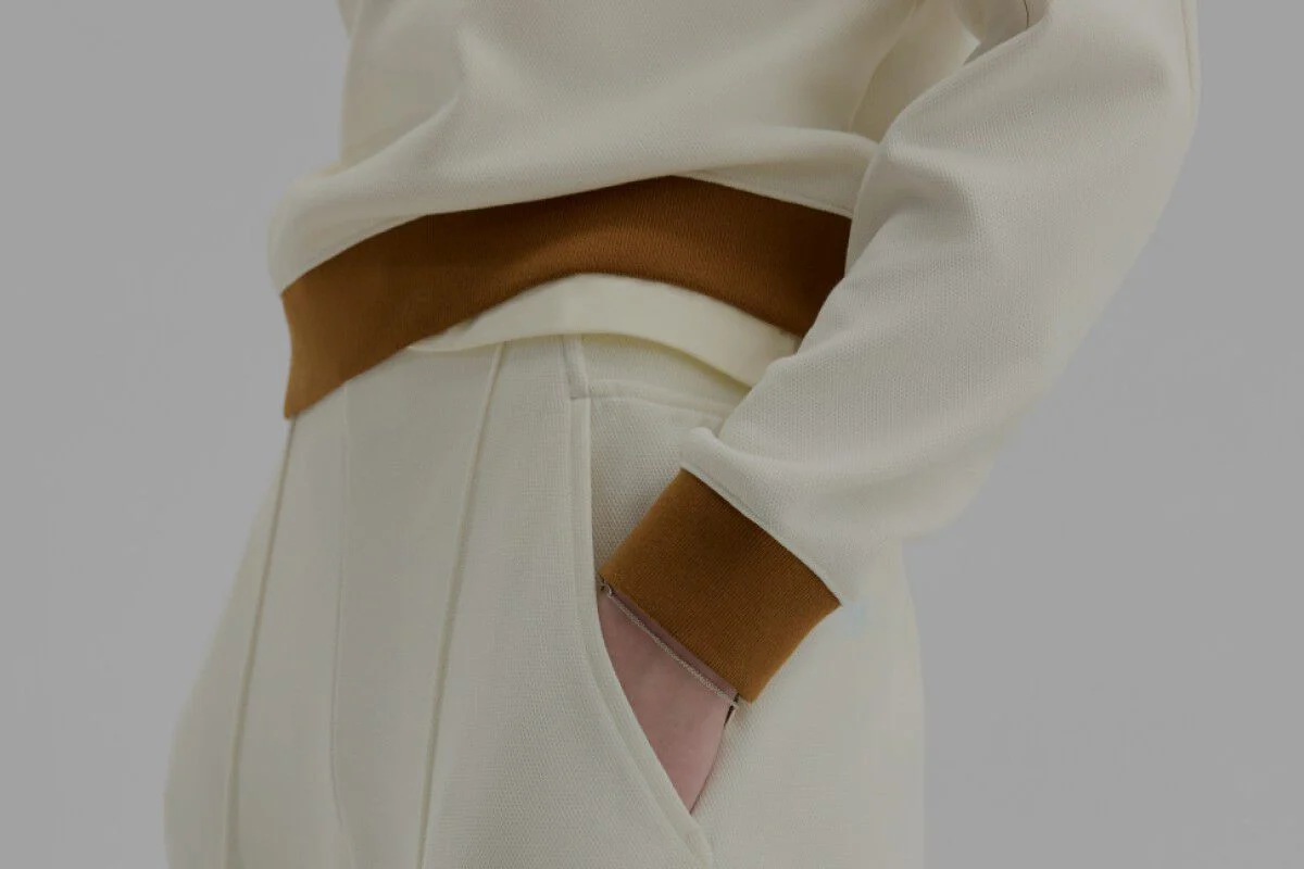 Close-up of someone wearing cream and brown New Balance pants on a white background. 
