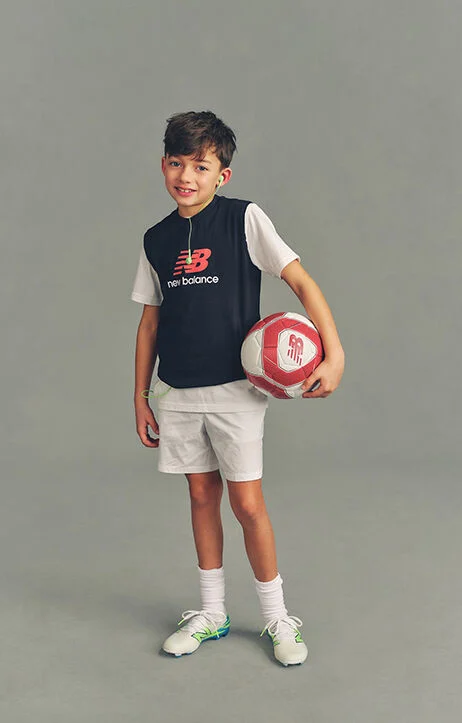 Kid holding a soccer ball against a grey studio background.