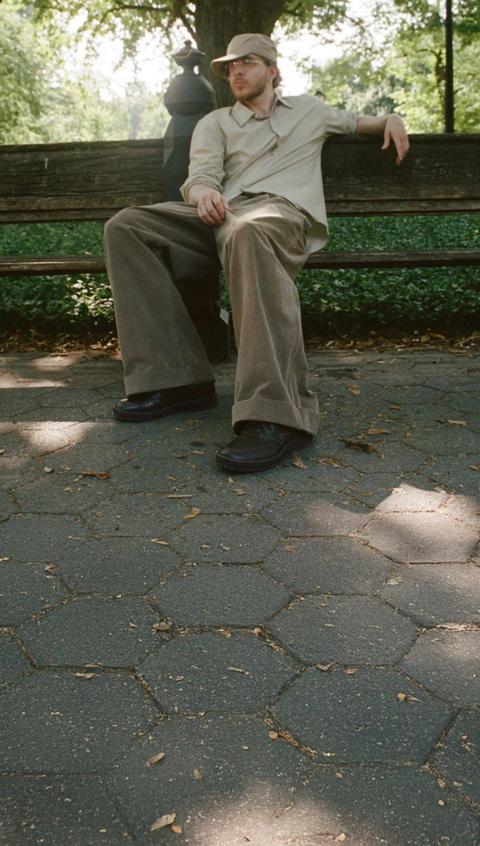 Jack Harlow reclining outside on a bench wearing dark brown New Balance sneakers.