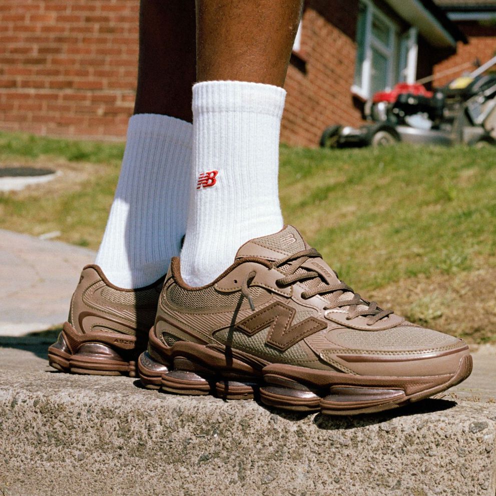 Imagen de rodilla hacia abajo de alguien que lleva unas zapatillas New Balance marrones al aire libre.