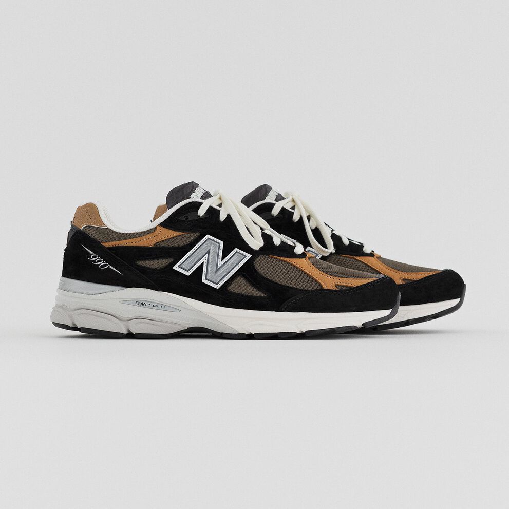 A pair of black and tan MADE in USA 990v3 on a grey studio backdrop.
