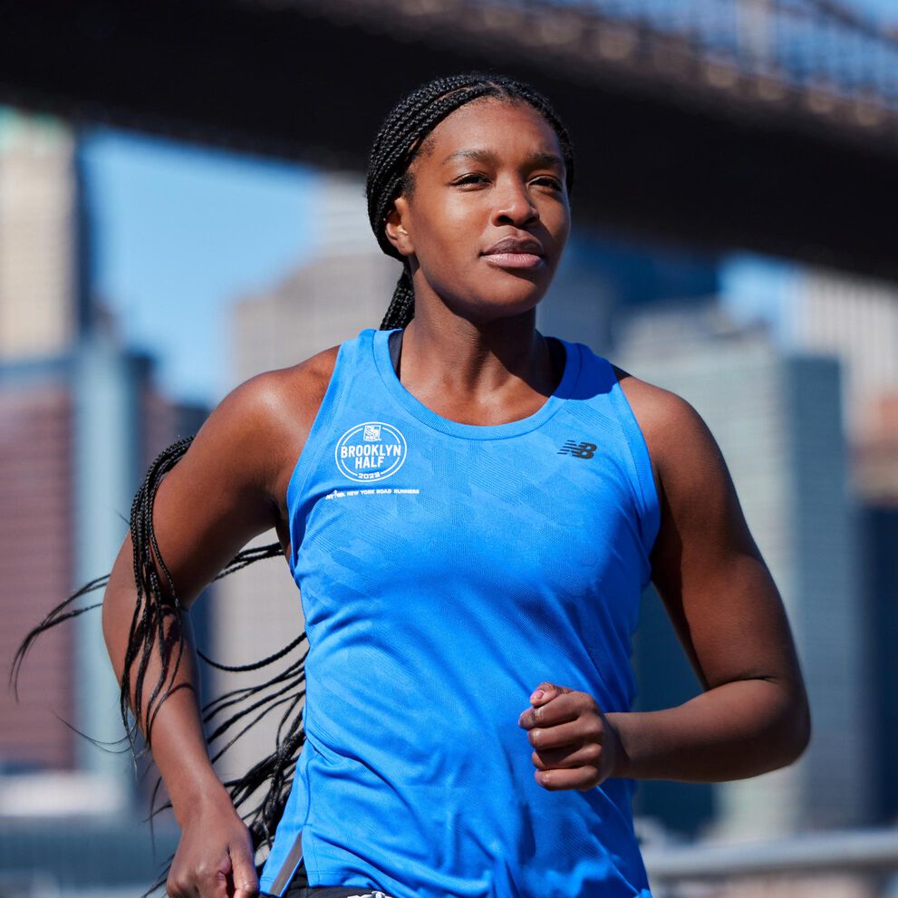 An individual in a blue New Balance tank top running in front of a city skyline. 