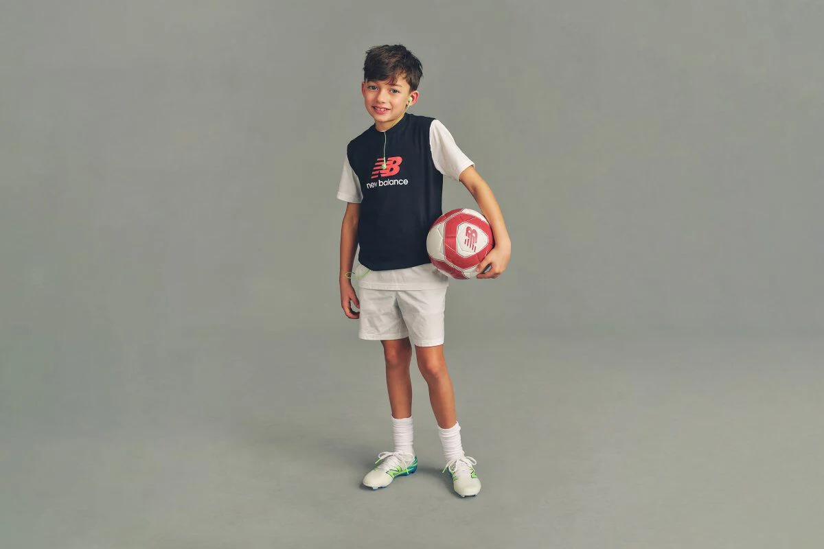 Imagen de estudio en primer plano de un ni&ntilde;o con una sudadera azul marino con capucha y el logo "New Balance Running" impreso en el pecho.