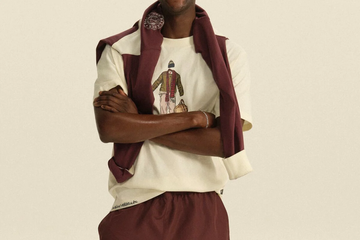 Person wearing a cream graphic T-shirt with a burgundy sweatshirt draped over the shoulders and matching athletic pants in a clean studio setting.