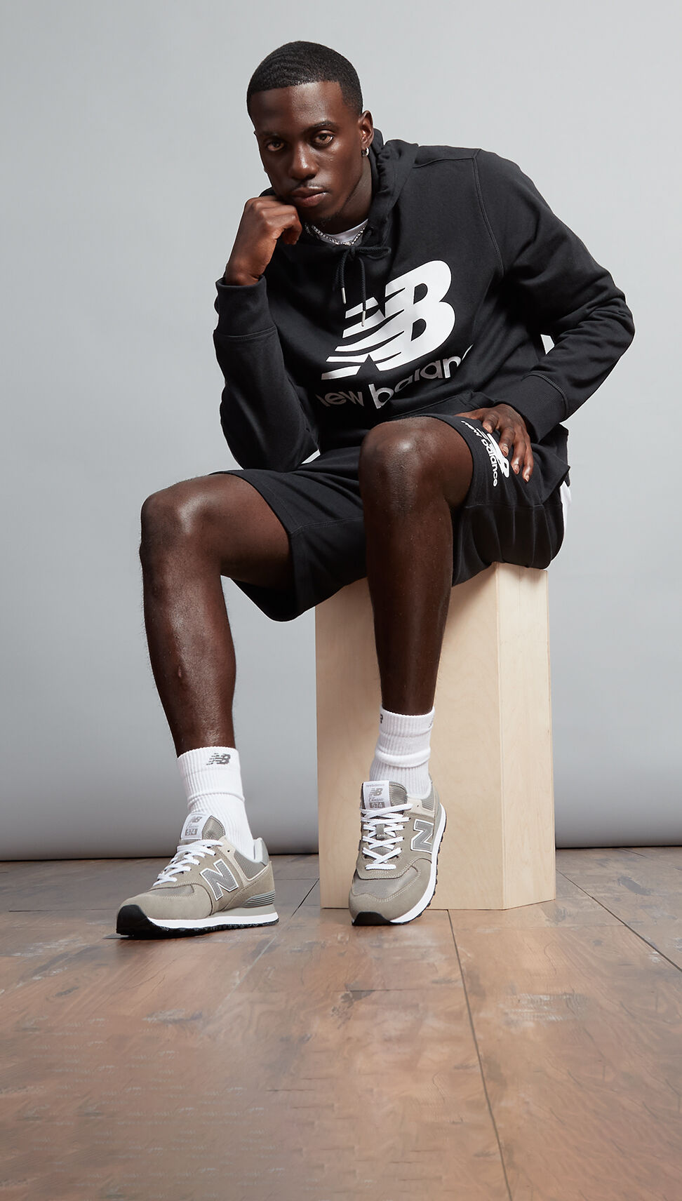 Soccer star in a black NB essentials hoodie sitting on a wooden stool.  
