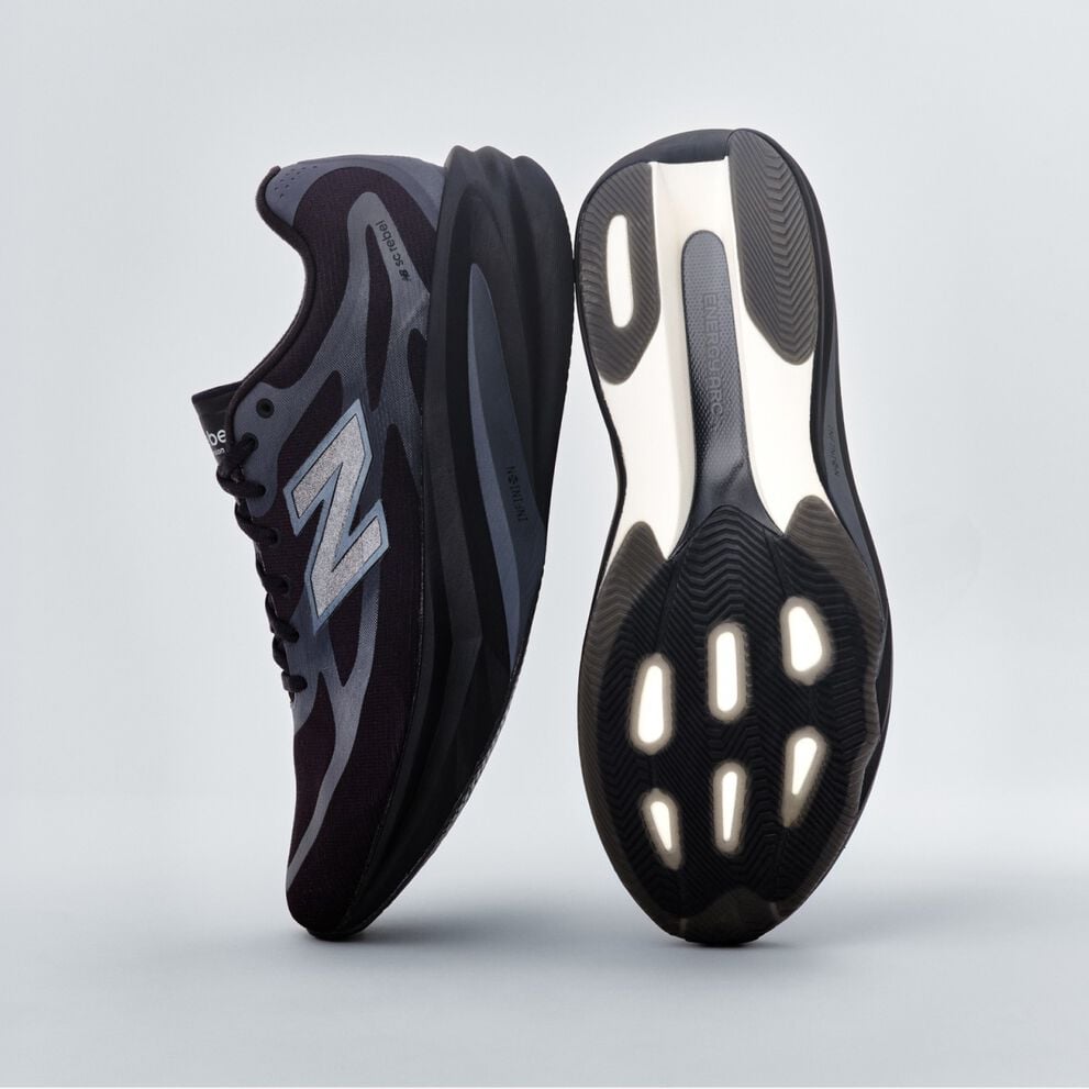 A pair of black New Balance sneakers sitting on a gray studio backdrop. 