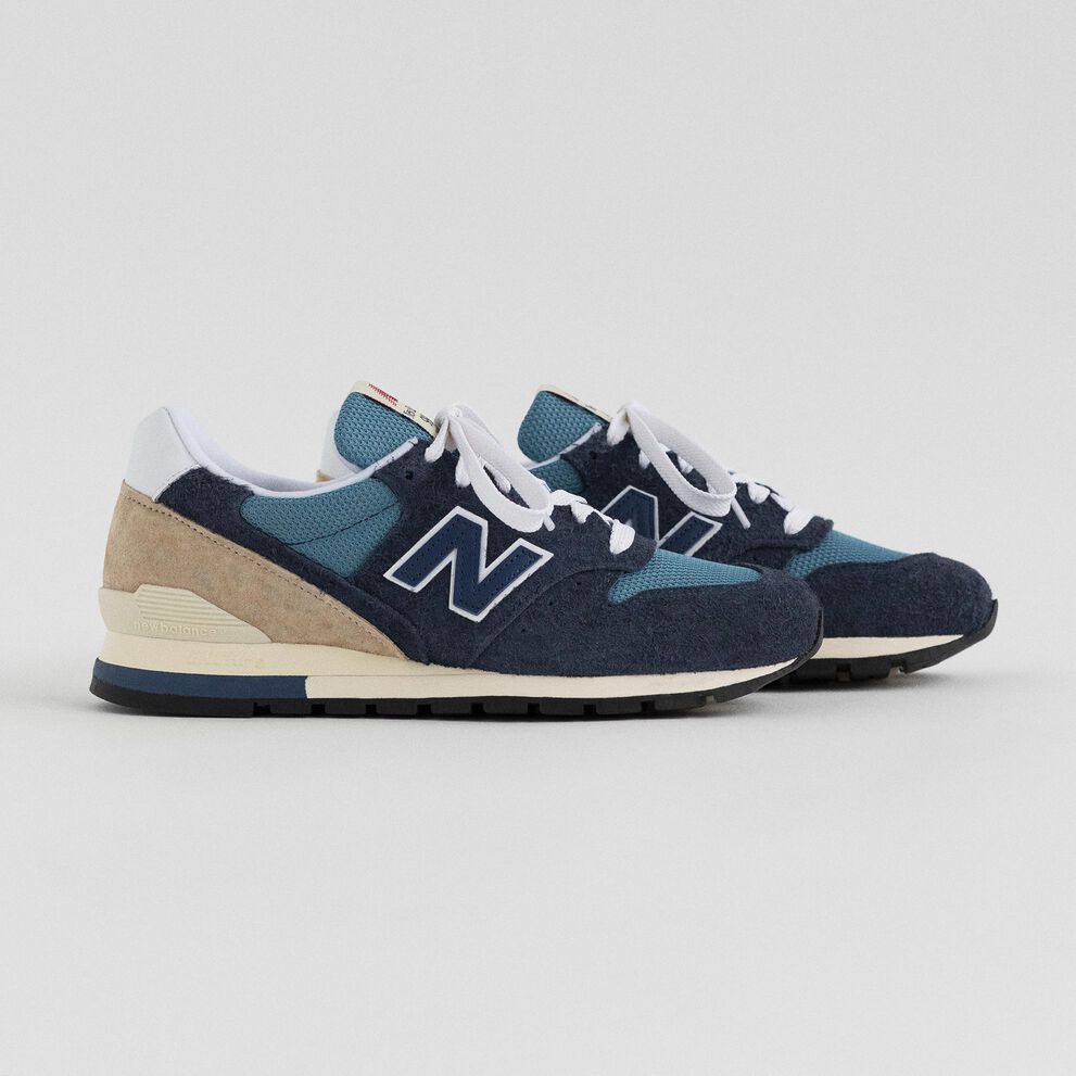 A pair of navy MADE in USA 996 sneakers on a grey studio backdrop. 